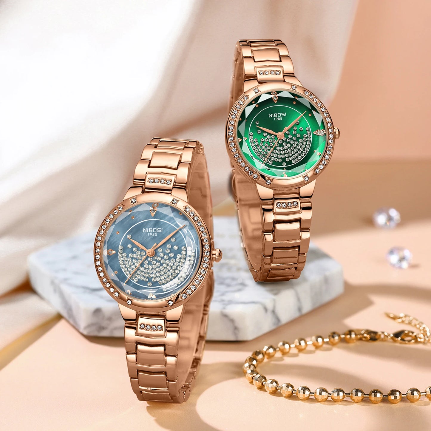 Two rose gold watches with green and blue faces on a marble surface.