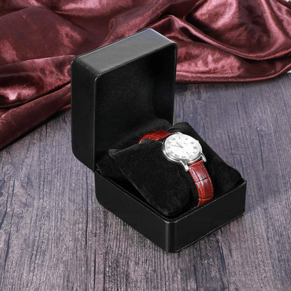 Watch with a brown leather strap in a black box on a wooden surface with red fabric in the background