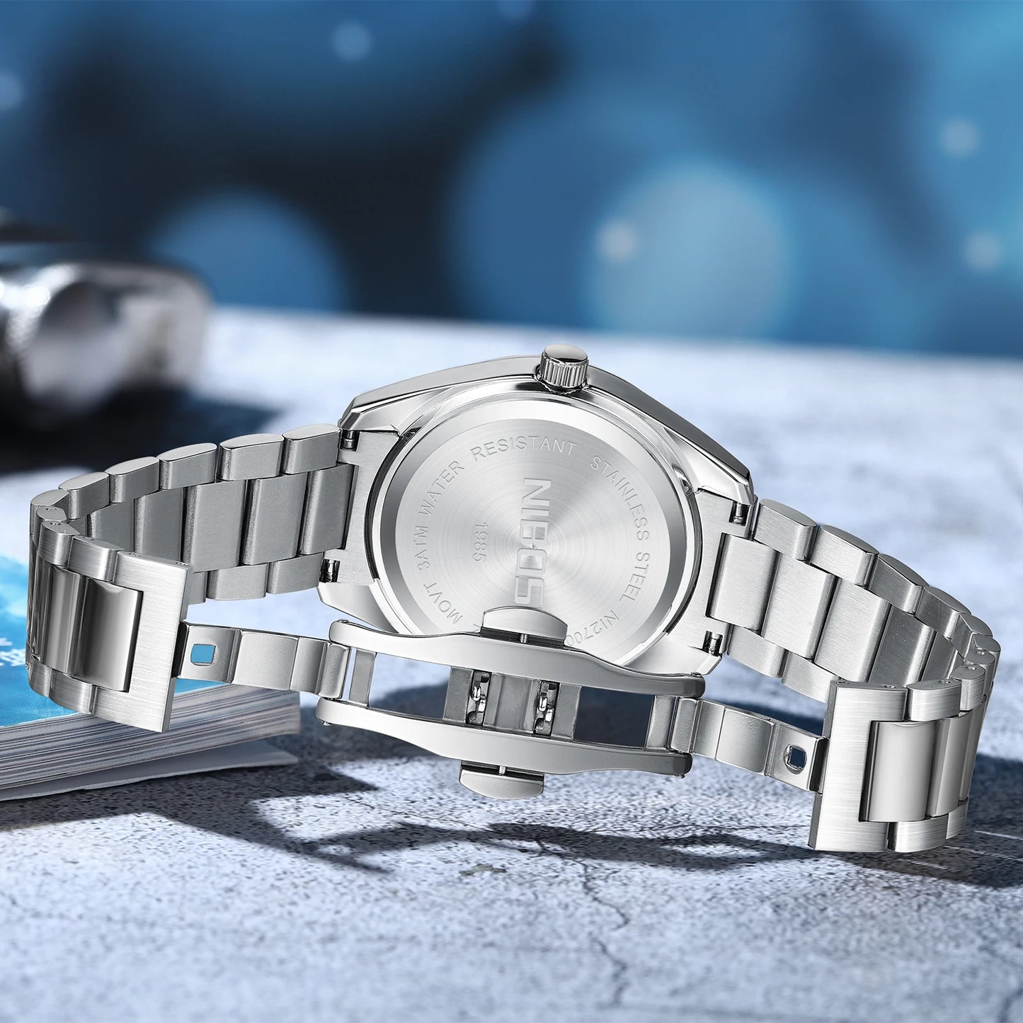 Silver watch with metal band on a textured surface with blue blurred background