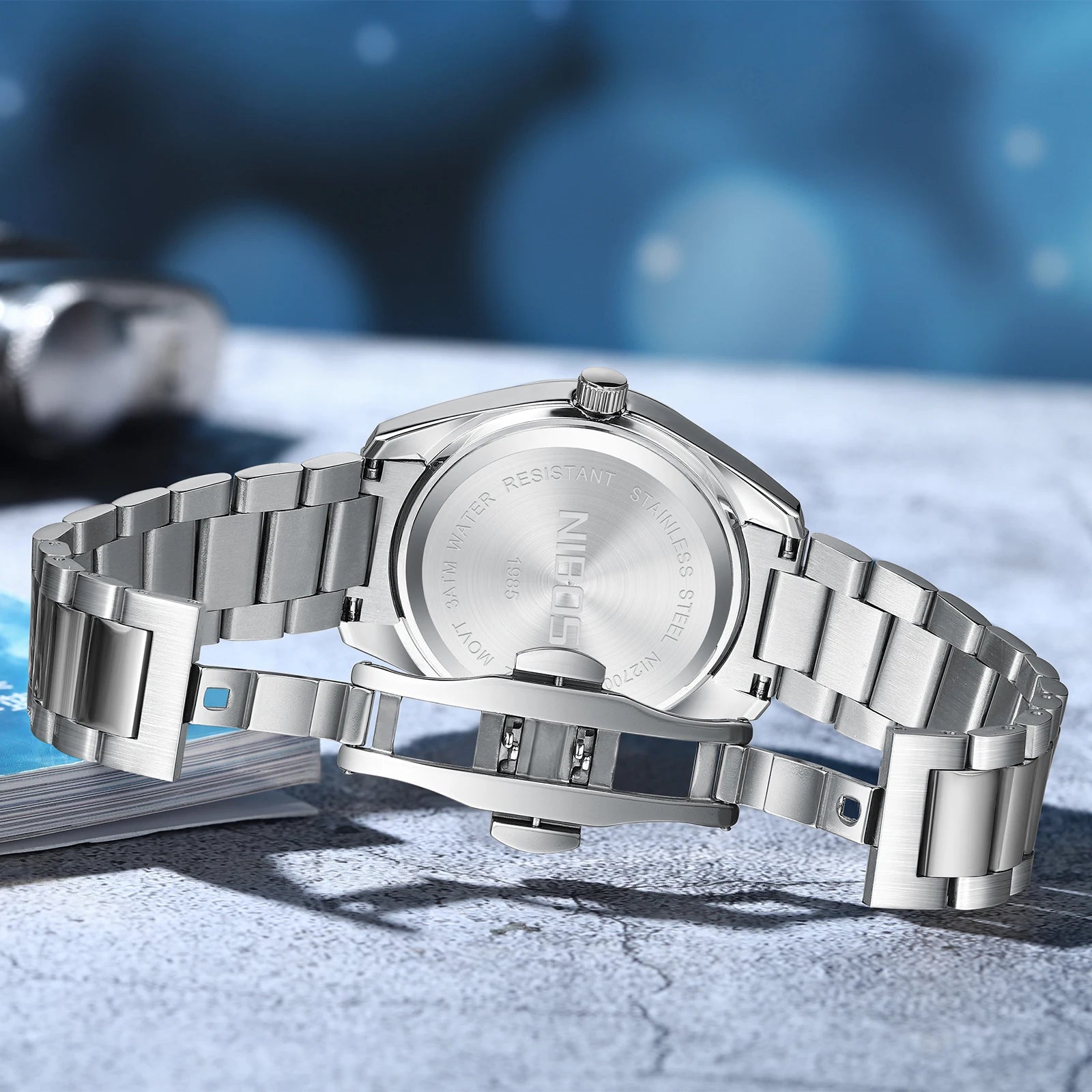 Silver watch with metal band on a textured surface with blue blurred background