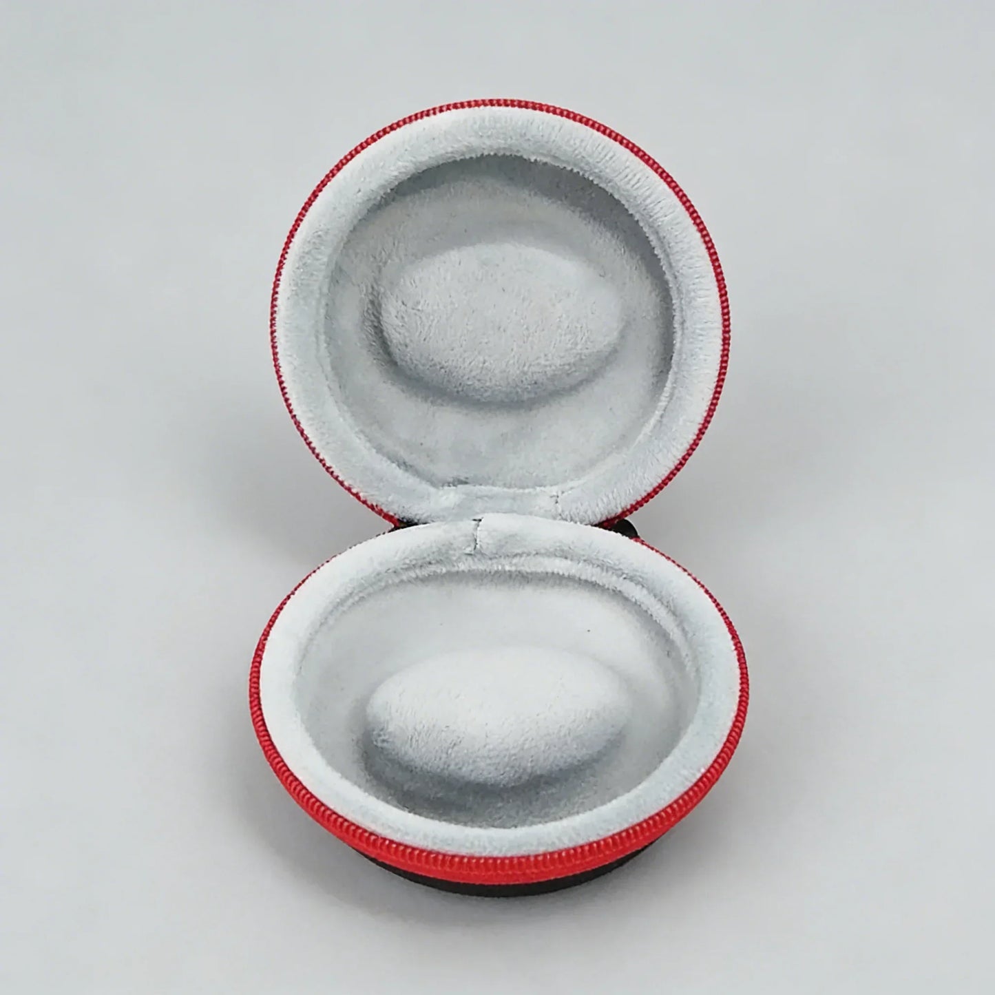 Round gray earbud case with red trim on a light gray background