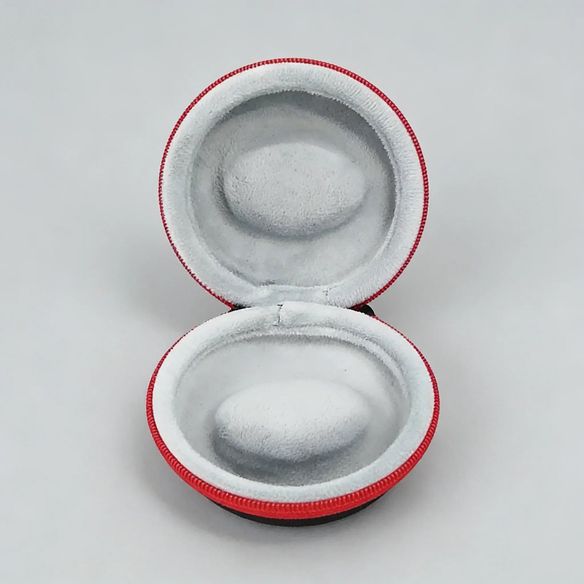 Round gray earbud case with red trim on a light gray background