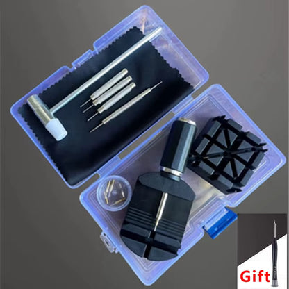 A watch or instrument repair kit shown open on a dark gray background, with multiple metal screwdriver bits, a small hammer, a black cleaning cloth, small screws, and a black plastic stand inside a translucent plastic case. A small 'Gift' label appears in the bottom-right corner.