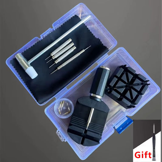 A watch or instrument repair kit shown open on a dark gray background, with multiple metal screwdriver bits, a small hammer, a black cleaning cloth, small screws, and a black plastic stand inside a translucent plastic case. A small 'Gift' label appears in the bottom-right corner.