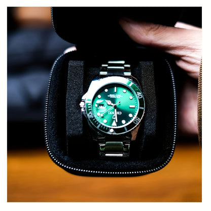 Green wristwatch in a black display case held by a person.