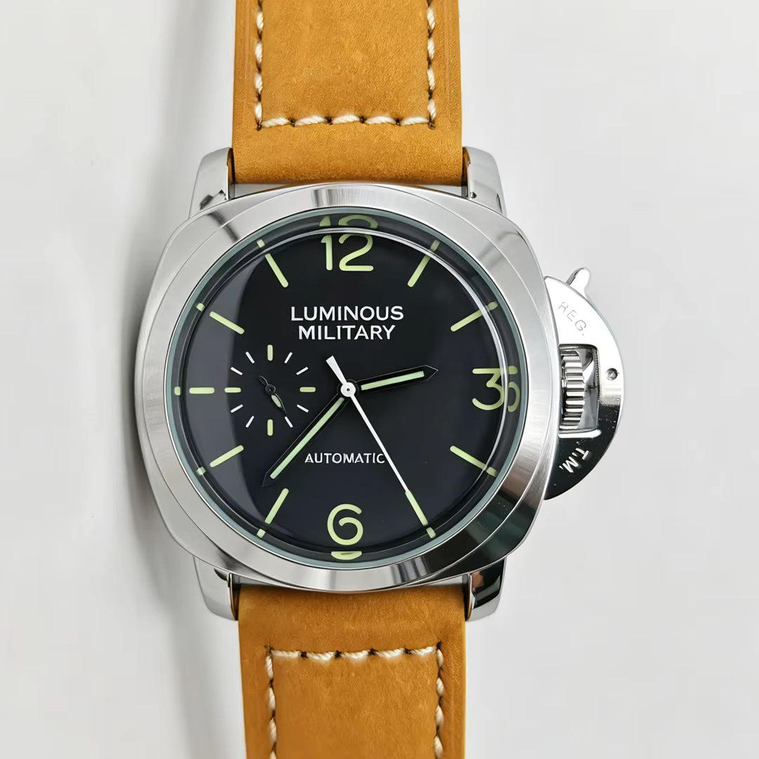 A close-up of a wristwatch with a tan leather strap, a silver-tone case, and a black dial featuring luminous green numerals and hands. The text 'LUMINOUS MILITARY' is visible on the dial.