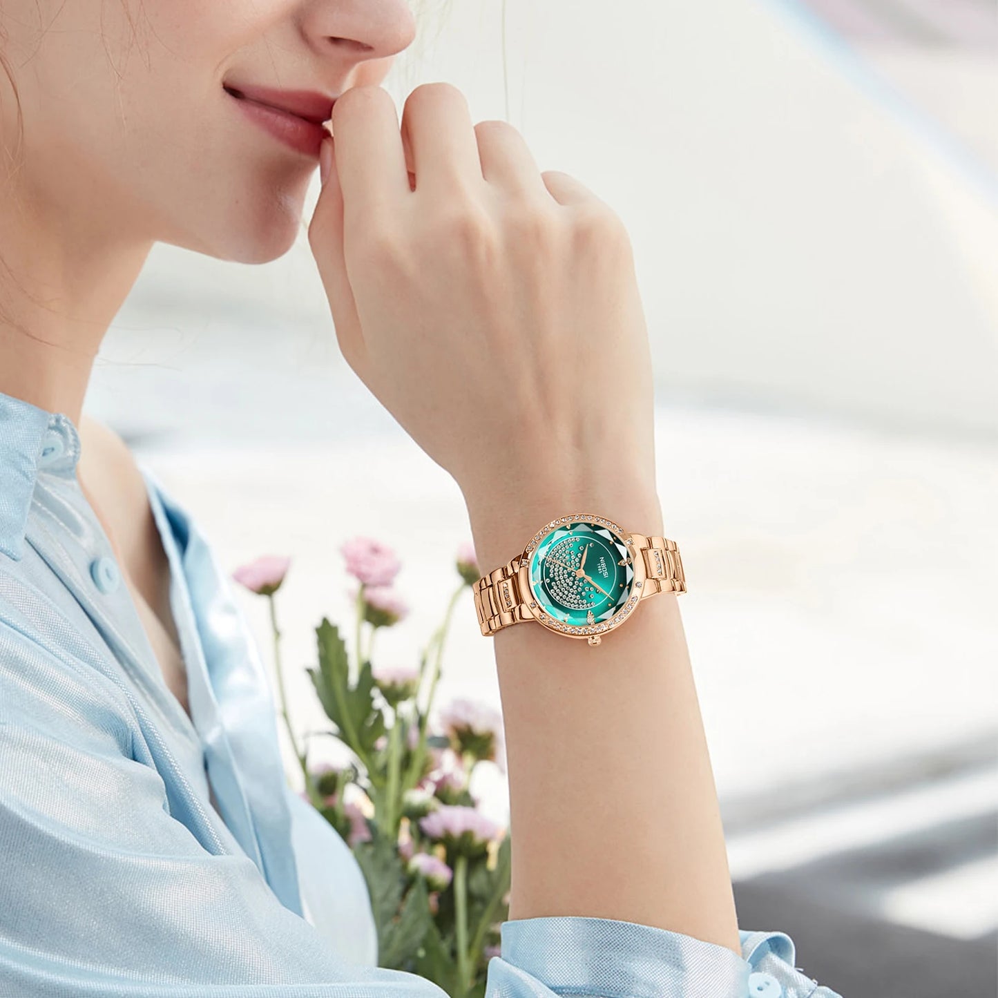 Woman wearing a rose gold watch with a green face, blurred flowers in the background
